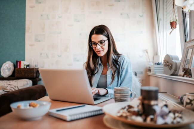 Happy young woman studying on laptop at her apartment.